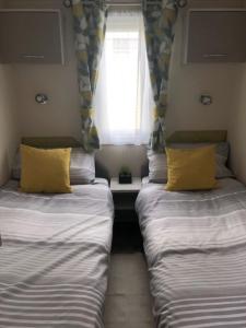 two beds with yellow pillows in a room with a window at AMETHYST 25 in Whitstable