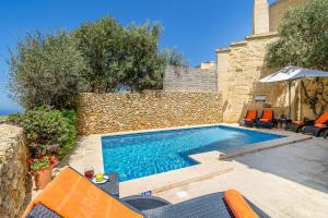 einen Pool mit orangefarbenen Stühlen und einer Steinmauer in der Unterkunft Hamlet 1 Holiday Home in Għasri