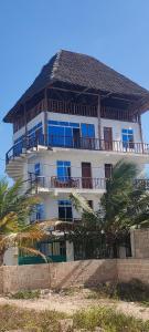 a large white building with blue windows and palm trees at Mambo Boutique Nungwi in Nungwi
