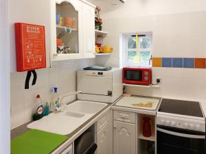 una pequeña cocina con armarios blancos y microondas rojo en The Gingang en Hexham
