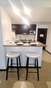 una cocina con 2 taburetes blancos y una barra en Ecusuites Empresarial Torre Sol II & Torre Medica 98, en Guayaquil