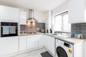 a kitchen with white cabinets and a washer and dryer at Cosy 2-Bed House! Dagenham! Free parking in Dagenham