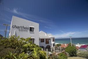 a white building with a sign on it next to the ocean at Chartfield Guesthouse in Kalk Bay