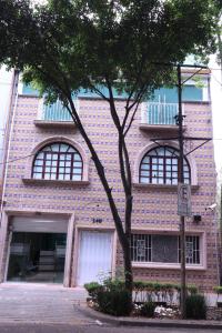 a brick building with three windows and a tree at London 248 in Mexico City