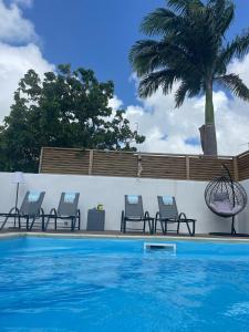 een zwembad met drie stoelen en een palmboom bij NOUVEAU Villa Ricololo Piscine Balnéo Golf Yoga in Saint-François