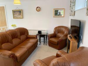 sala de estar con sofás de cuero y TV en Rosebank Cottage, en Aldbrough