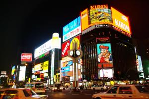 una strada trafficata di notte con auto e cartelli di The Base Sapporo Susukino a Sapporo