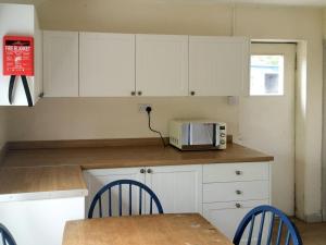 cocina con armarios blancos, mesa y microondas en Cauldside West Cottage en Whitekirk