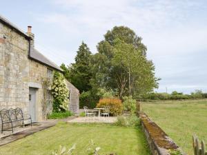 an old stone house with a garden and a table at Greenyard Cottage in Rothbury