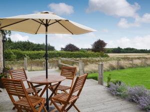 een tafel en stoelen met een parasol op een houten terras bij Little Barn Tynely Farm in Ellingham