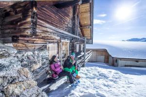 dos mujeres sentadas fuera de una cabaña en la nieve en Hotel Landhaus Zillertal en Fügen