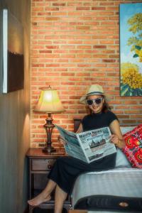 a woman sitting on a bed reading a newspaper at Nan De Panna Resort and Spa in Nan