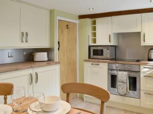 a kitchen with white cabinets and a table with wine glasses at Fern Cottage in Bradwell