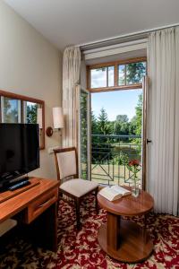 ein Hotelzimmer mit einem Schreibtisch, einem TV und einem Fenster in der Unterkunft Hotel Violeta in Druskininkai