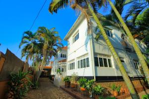 een wit huis met palmbomen ervoor bij Ambassador Bridge Motel in Jinja