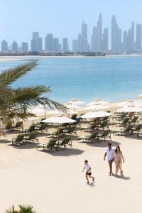 two people walking on a beach with surfboards at Raffles The Palm in Dubai
