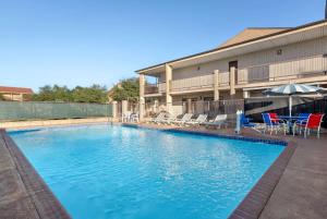 a swimming pool in front of a building with chairs and an umbrella at Ramada by Wyndham San Antonio Near SeaWorld - Lackland AFB in San Antonio