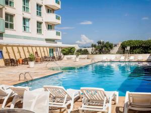 uma piscina com cadeiras e um edifício em Mercure Macae em Macaé