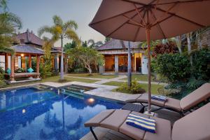 a swimming pool with an umbrella and chairs next to a house at Askara Villa in Canggu