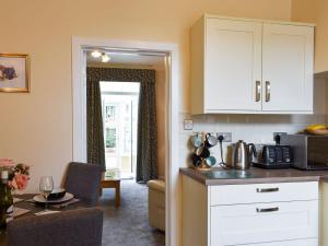 a kitchen with white cabinets and a dining room with a table at End Cottage in Alnwick