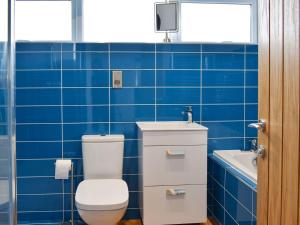 a blue tiled bathroom with a toilet and a sink at Chapel Farm Barn in Smeeth