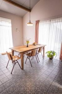 una mesa de madera con sillas en una habitación con ventanas en De Kaasmakerij - Ruim vakantiehuisje op Huize Blokland en Hem