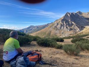 un hombre sentado en una colina con una mochila en Los Chozos de la Braña, en Brañosera