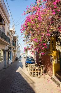 a street with tables and chairs under a tree with pink flowers at MATILDA Central Apartment in Aegina Town