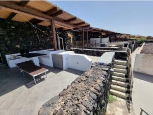 un patio con pared de piedra, mesa y banco en Perla Nera I DAMMUSI DI SCAURI en Pantelleria