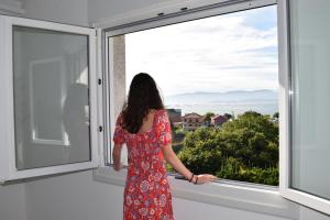 une femme en robe rouge qui regarde par une fenêtre dans l'établissement Apartamento Corcubica mirando al mar, à Vilagarcía de Arousa