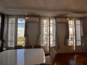 uma sala de jantar com uma mesa branca e janelas grandes em Appartement Champs-Élysées - HALA PARIS em Paris