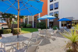un patio avec des tables et des chaises et des parasols bleus dans l'établissement Best Western Plus Wilmington / Wrightsville Beach, à Wilmington