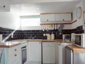 a kitchen with white cabinets and a black tiled wall at Paramount Cottage in Farden