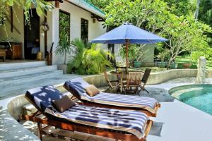 2 sedie a sdraio e un ombrellone accanto alla piscina di Villa Serene & Spa Mangsit a Mangsit