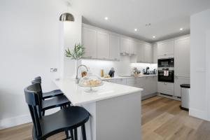 a kitchen with white cabinets and a counter with chairs at Design-Led Luxurious Townhouse Prime Location W/ Parking in Reading