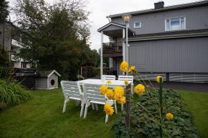 une table et des chaises blanches dans une cour ornée de fleurs jaunes dans l'établissement Käytännöllinen huoneisto Pietarsaaressa, à Pietarsaari