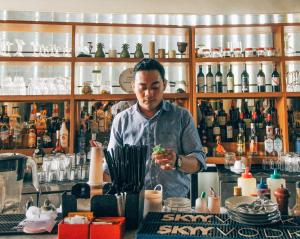 un homme debout derrière un comptoir dans un bar dans l'établissement Grandmas Plus Hotel Seminyak, à Seminyak