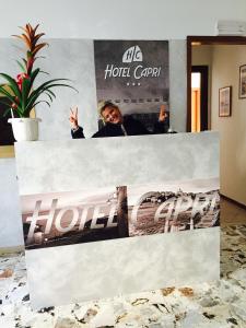 a man giving the peace sign while standing behind a hotel sign at Hotel Capri in Diano Marina