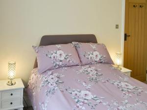 a bed with a pink bedspread with flowers on it at Dollys Cottage in Ovingham