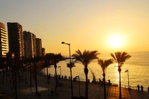 einen Strand mit Palmen und dem Meer bei Sonnenuntergang in der Unterkunft Bayview Hotel Beirut in Beirut