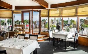 a restaurant with white tables and chairs and large windows at Hotel Dom Zdrojowy Resort & SPA in Jastarnia