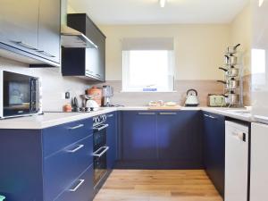 una cucina con armadi blu e banconi bianchi di Half House a Nethy Bridge