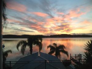 una puesta de sol sobre un lago con palmeras y una casa en Overnight Reflections B&B, en Fishing Point