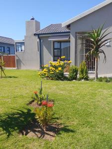 a yard with a house and some flowers in the grass at Droom Verlore in Jeffreys Bay