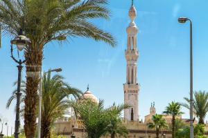 a mosque with a tall tower and a palm tree at Royal Hotel in Qena