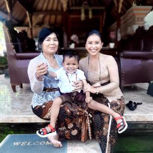 two women and a child sitting on a bench at Odah Ayu Guest House in Ubud