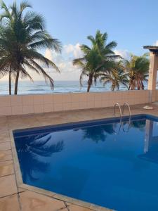 a swimming pool with palm trees and the ocean at Quarto particular na praia do flamengo in Salvador