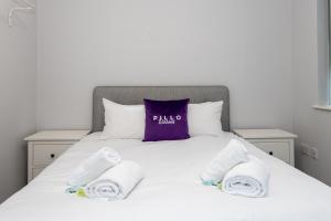 a bed with towels on it with a purple pillow at Pillo Rooms Serviced Apartments - Trafford in Manchester