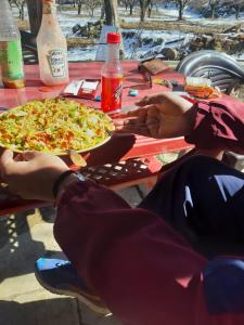 a group of people sitting at a picnic table with two pizzas at Evergreen Café in Kalgha
