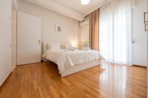 a white bedroom with a bed and a wooden floor at Διαμέρισμα 55 τ.μ. στο κέντρο με δωρεάν πάρκινγκ in Larisa